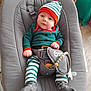accessory, baby, baby_rocker, child, clothing, cute, elf_costume, festive_outfit, gray_fabric, hat, indoor, infant, pacifier, pacifier_clip, person, seated, smiling, striped_clothing, toy, wooden_floor