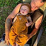 baby, child, adult, tattoos, overalls, beanie, outdoor, grass, lawn_chair, table, can, sunlight, person, casual_clothing, greenery, relaxation, barefoot, summer, portrait, family