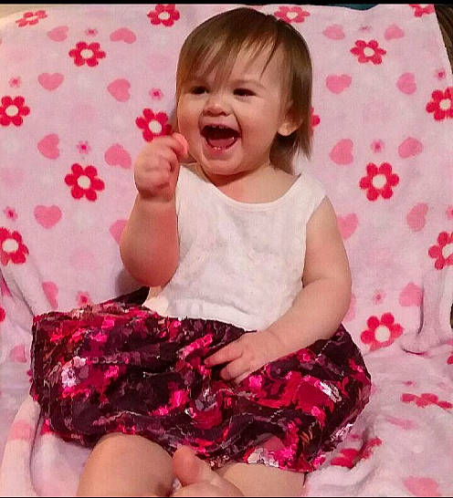 Adelynn is registered to the contest to win money with this photo: baby, baby_toddler_clothing, cheek, child, dress, facial_expression, finger, gesture, happy, laugh, leg, mouth, person, pink, sitting, skin, sleeve, smile, toddler