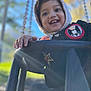 Elyas participe au concours pour gagner de l'argent avec cette photo : child, toddler, swing, outdoor, smiling, hood, jacket, sunlight, playground, happy, hand, face, trees, daylight, park, young, fun, person, clothing, nature