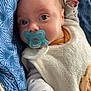 baby, infant, newborn, pacifier, face, eyes, hand, bib, onesie, blanket, blue_pattern, fabric, close_up, portrait, indoors, cozy, soft_texture, cute, sleepy, comfort