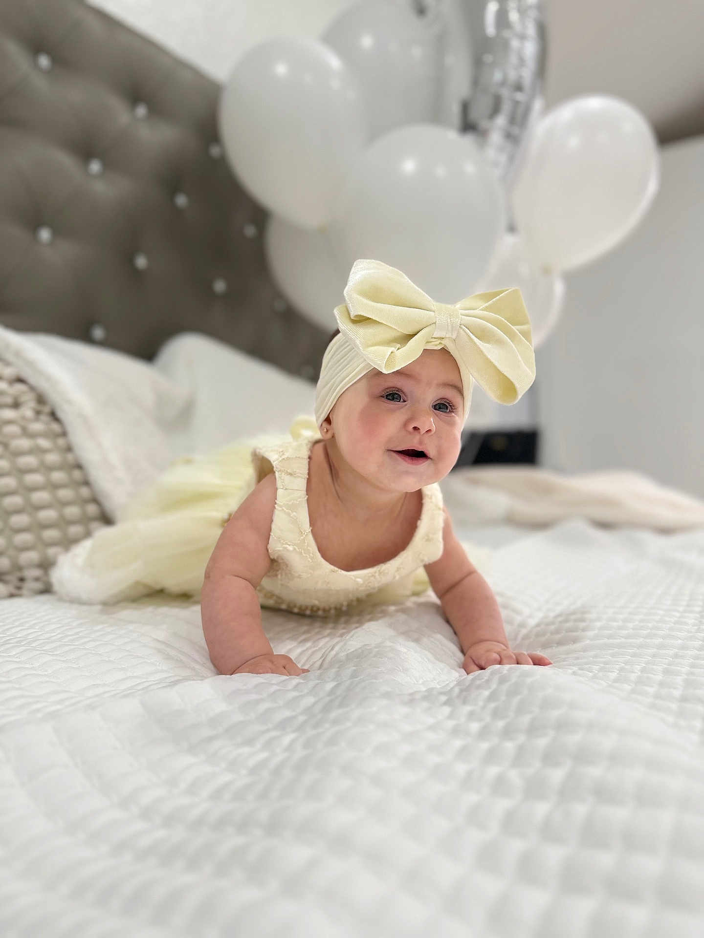 Aliah is registered to the contest to win money with this photo: baby, child, crawling, bed, white_bedspread, balloons, headband, bow, dress, pillow, indoor, cute, smiling, happy, infant, portrait, soft_lighting, fabric, celebration, decor