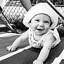 Isaiah is registered to the contest to win money with this photo: baby, child, smiling, hat, crawling, outdoor, mat, fence, black_and_white, cute, happy, infant, face, person, sunlight, texture, playful, clothing, headwear, expression