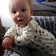 Isaiah joined the competition — help win amazing prizes! baby, infant, onesie, blanket, knitted_blanket, indoor, child, person, couch, carpet, curious, face, hand, sitting, home, cozy, soft_lighting, background, toy, cap