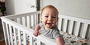 Isaiah joined the competition — help win amazing prizes! baby, crib, smiling, infant, striped_clothing, animal_print, mattress, white_crib, hand, face, indoor, wooden_floor, door, doorknob, nursery, child, cute, happy, person, playful