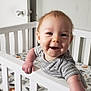 baby, crib, smiling, infant, striped_clothing, animal_print, mattress, white_crib, hand, face, indoor, wooden_floor, door, doorknob, nursery, child, cute, happy, person, playful