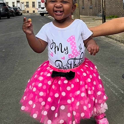 Meilanilee is registered to the contest to win money with this photo: toddler, child, birthday, pink_skirt, polka_dots, shoes, smile, happy, urban, street, sidewalk, daylight, person, clothing, hair_bows, celebration, first_birthday, outdoor, standing, support