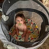 baby, pacifier, playpen, colorful_mat, geometric_pattern, indoor, carpet, child, sitting, curious, cute, infant, soft_lighting, head, face, brown_hair, diaper, toy_area, furniture, home