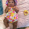 baby, infant, child, smiling, happy, portrait, floral_outfit, sun_hat, colorful_clothing, lying_down, bed, blanket, pink, toy, mirror, indoor, home, bare_legs, socks, photography