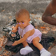 Yazmin is registered to the contest to win money with this photo: baby, child, outdoor, grass, sneakers, purple_outfit, jewelry, pacifier, cup, bag, person, trees, sidewalk, fall_leaves, playing, cute, accessories, sunlight, blurred_background, purple_butterflies