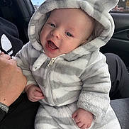 Asher is registered to the contest to win money with this photo: baby, infant, child, onesie, hood, bear_ears, striped_clothing, smiling, happy, hand, adult, car_interior, window, seat, person, face, cute, soft_texture, warm_clothing, portrait