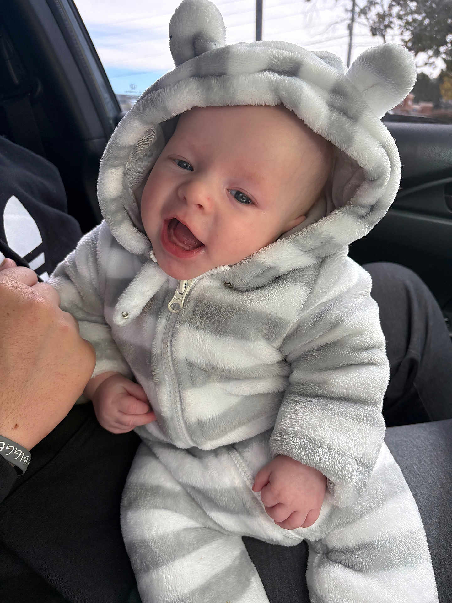 Asher is registered to the contest to win money with this photo: baby, infant, child, onesie, hood, bear_ears, striped_clothing, smiling, happy, hand, adult, car_interior, window, seat, person, face, cute, soft_texture, warm_clothing, portrait