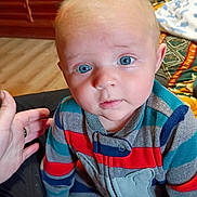 Anthony joined the competition — help win amazing prizes! baby, child, blue_eyes, striped_clothing, onesie, indoor, living_room, television, hand, floor, blanket, carpet, person, seated, curious_expression, casual, home, cute, infant, portrait