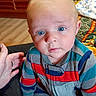 baby, child, blue_eyes, striped_clothing, onesie, indoor, living_room, television, hand, floor, blanket, carpet, person, seated, curious_expression, casual, home, cute, infant, portrait