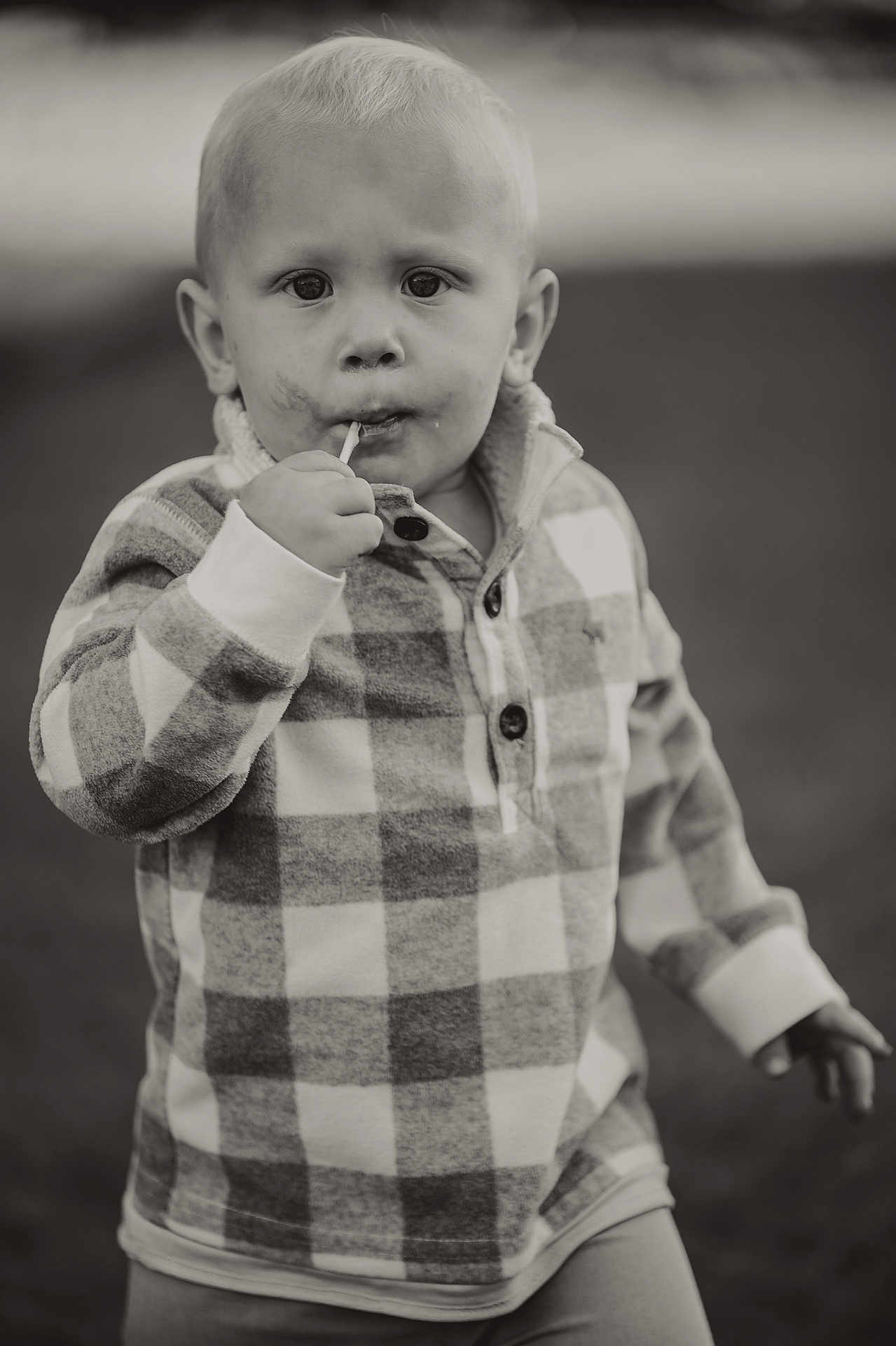 Seanpaul is registered to the contest to win money with this photo: child, toddler, plaid_shirt, lollipop, outdoor, portrait, face, curious, blond_hair, smudge, long_sleeves, young_child, standing, casual_clothing, expression, person, monochrome, black_and_white, close_up, cute