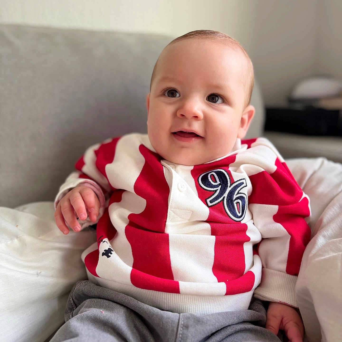 Giulio participe au concours pour gagner de l'argent avec cette photo : baby, child, infant, face, person, clothing, red, white, striped_shirt, number_96, couch, cushion, indoor, smiling, happy, sitting, portrait, head, hand, cozy