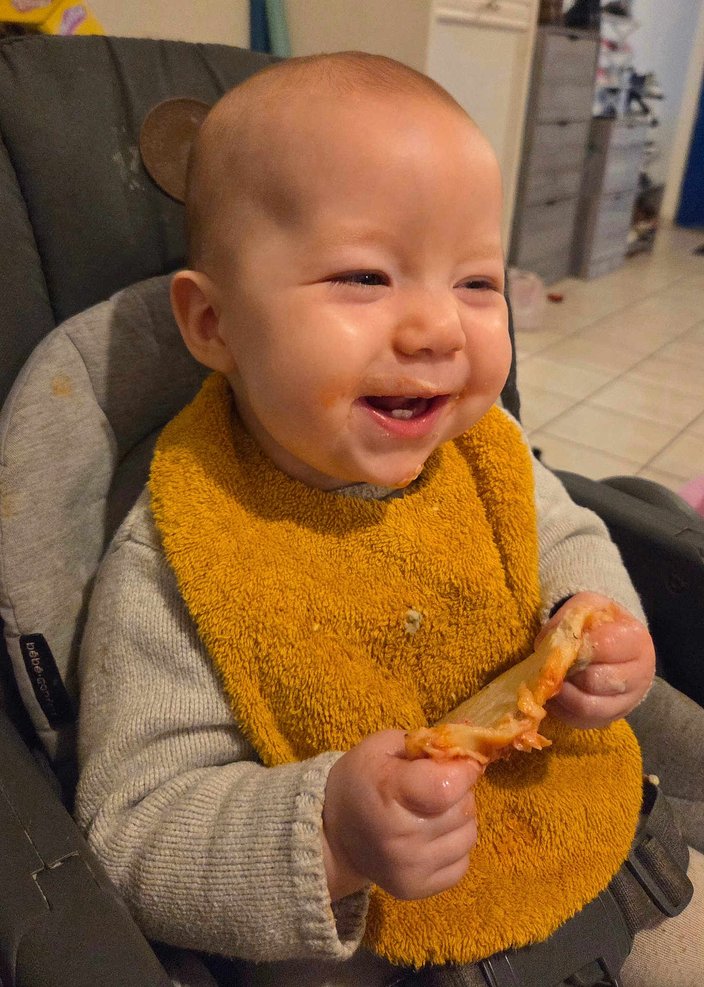 Azelie participe au concours pour gagner de l'argent avec cette photo : baby, infant, highchair, bib, food, eating, messy, smile, happy, hands, meal, indoor, kitchen, tile_floor, clothing, seat, closeup, face, teeth, cheese