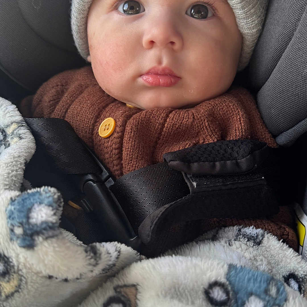 Itai joined the competition — help win amazing prizes! baby, child, face, hat, knit_hat, brown_sweater, blanket, car_seat, seatbelt, cozy, cute, indoors, portrait, wide_eyes, infant, warm_clothing, soft_texture, looking_up, snug, child_seat