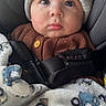 Itai is registered to the contest to win money with this photo: baby, child, car_seat, blanket, knit_hat, brown_sweater, face, eyes, seatbelt, infant, cute, warm_clothing, indoor, portrait, expression, cozy, patterned_blanket, car, safety_strap, young