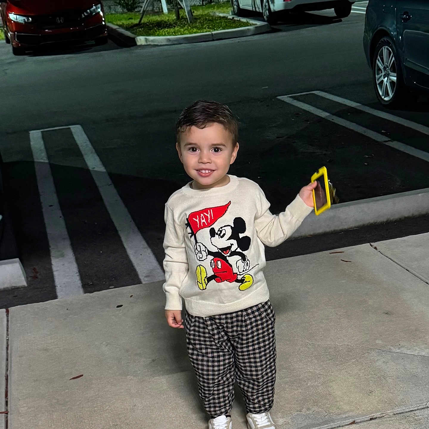 Mateo joined the competition — help win amazing prizes! toddler, child, smiling, mickey_mouse, sweater, checkered_pants, sneakers, sidewalk, night, parking_lot, car, fence, holding_phone, person, outdoor, happy, clothing, fashion, casual, urban