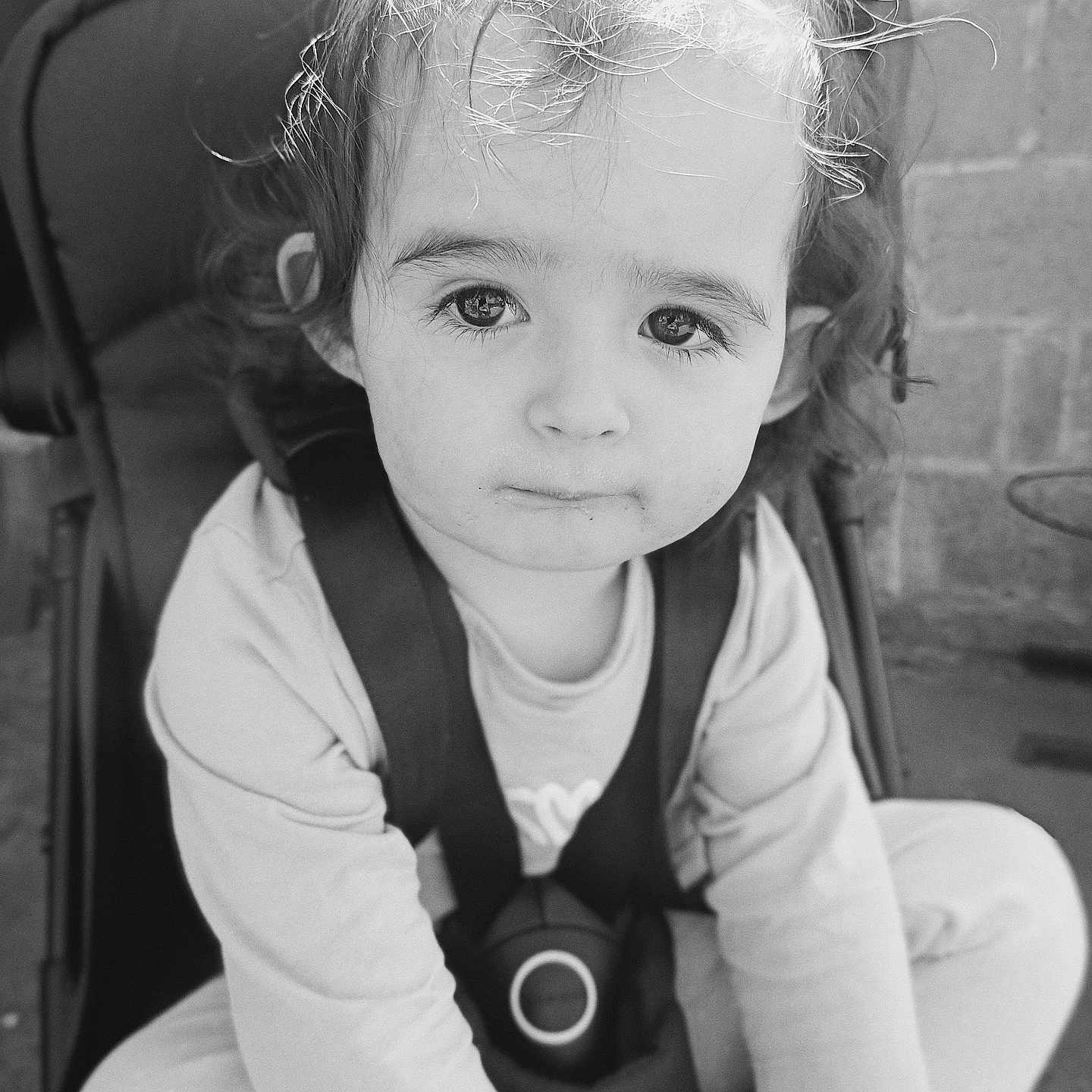 Luuna participe au concours pour gagner de l'argent avec cette photo : baby, black_and_white, candid, child, clothing, curly_hair, cute, expression, eyes, face, hair, long_sleeve, outdoor, person, portrait, seatbelt, sitting, stroller, toddler, young_child