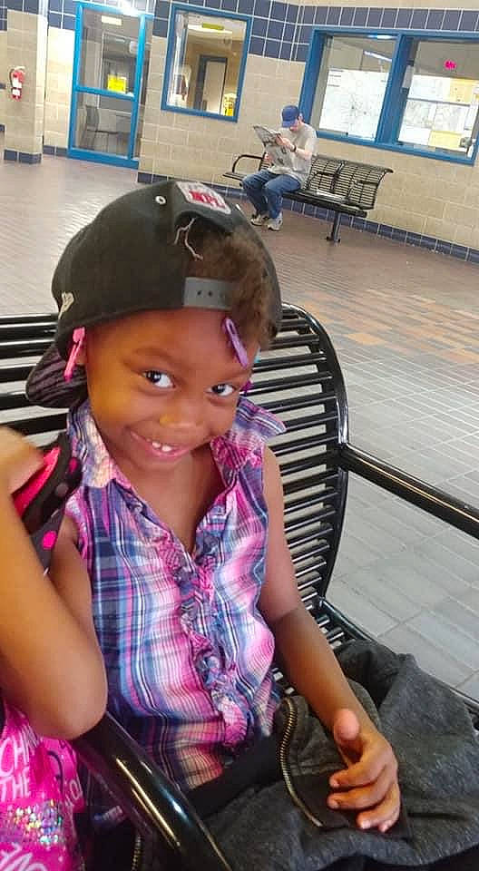 Khyree is registered to the contest to win money with this photo: baby_toddler_clothing, baseball_cap, bench, bracelet, cap, child_model, floor, flooring, headwear, joy, lap, person, pink, plaid, purple, sitting, tartan