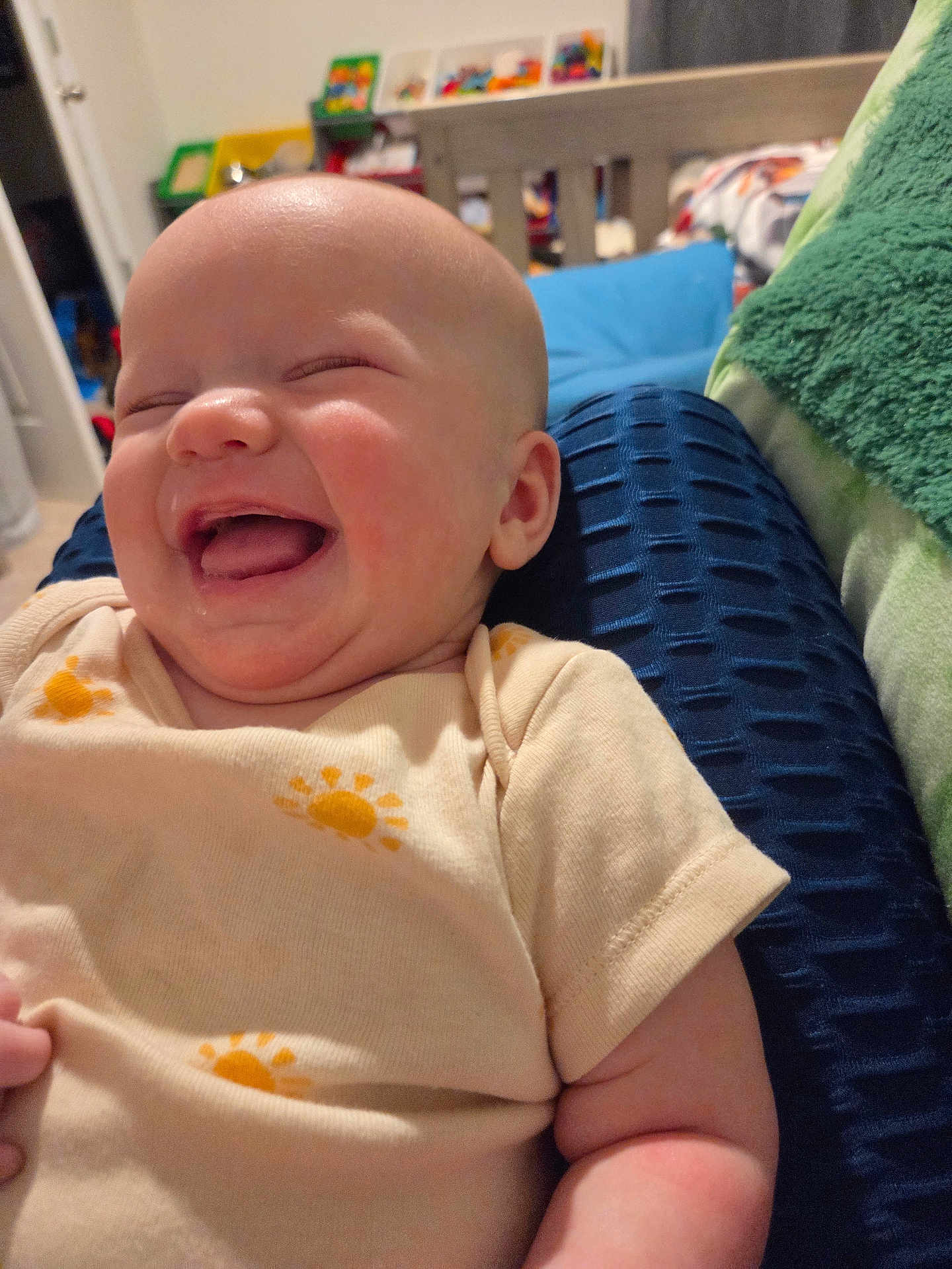 Makenzie is registered to the contest to win money with this photo: baby, infant, smiling, laughing, face, head, onesie, clothing, cheeks, drool, pillow, blanket, crib, nursery, toy_shelf, hand, closeup, indoor, happy, portrait