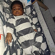 Ismael a rejoint le concours — aidez-le/la à gagner de superbes lots ! baby, infant, onesie, striped_clothing, blanket, cloud_pattern, nursery, bed, sleeping_area, soft_fabric, child, person, indoor, cute, young, resting, face, hand, footwear, plush