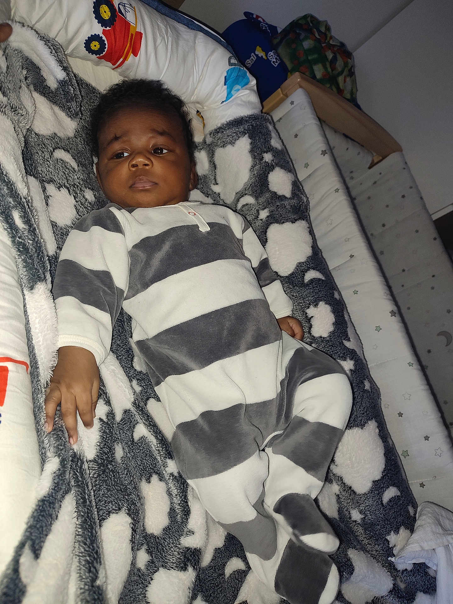 Ismael a rejoint le concours — aidez-le/la à gagner de superbes lots ! baby, infant, onesie, striped_clothing, blanket, cloud_pattern, nursery, bed, sleeping_area, soft_fabric, child, person, indoor, cute, young, resting, face, hand, footwear, plush