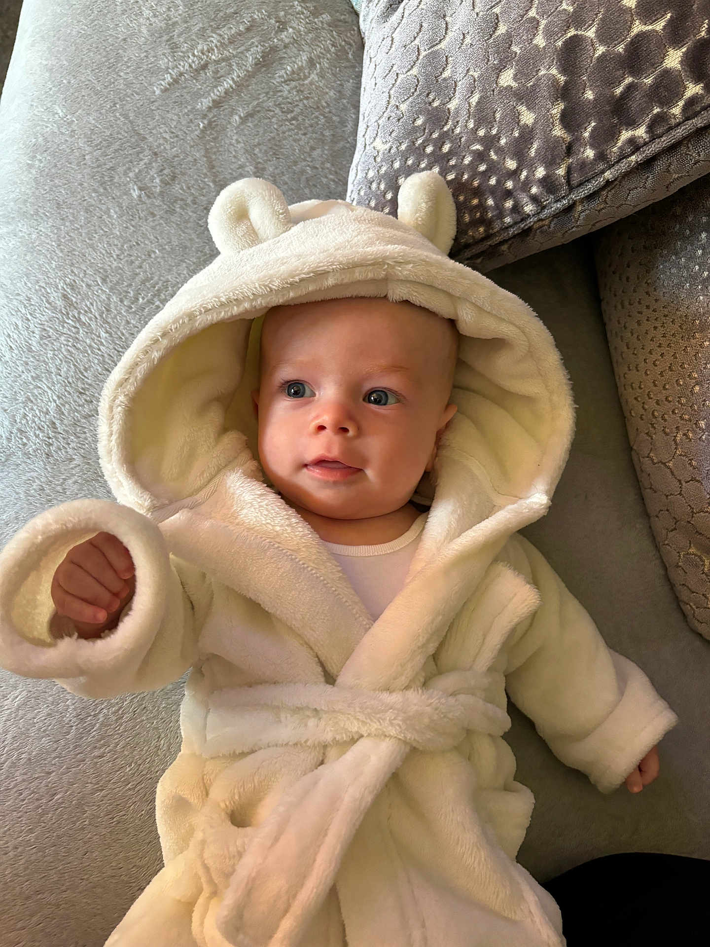 Ace joined the competition — help win amazing prizes! baby, infant, hooded_robe, white_clothing, couch, cushion, soft_texture, indoor, person, child, cute, cozy, portrait, smiling, furniture, relaxing, young_child, comfortable, warm, expression