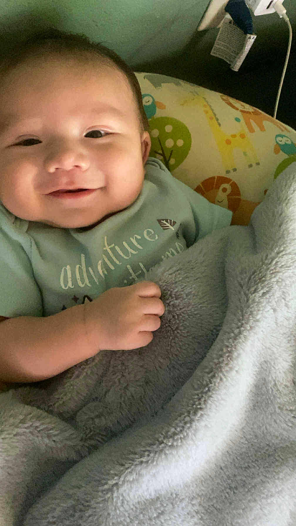 Kizer is registered to the contest to win money with this photo: baby, smile, blanket, pillow, animal_pattern, infant, cozy, happy, child, bed, soft, cute, wrapped, hand, face, indoors, comfort, green_background, clothing, resting