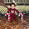toddler, child, pajamas, red_and_black, bear_design, candy_cane, lights, autumn_leaves, fence, tattooed_arm, nighttime, outdoor, holiday_decor, person, smiling, curly_hair, supporting_hand, festive, cozy, cute