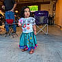 Gabriella is registered to the contest to win money with this photo: child, girl, traditional_clothing, colorful, garage, man, television, sports, chair, table, concrete_floor, shoes, curly_hair, watching, indoor, casual, family, candid, bowl, standing