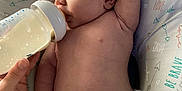 Wayden is registered to the contest to win money with this photo: baby, infant, bottle, feeding, diaper, hand, pillow, pattern, arrows, text, love, be_brave, lying_down, skin, arm, face, head, person, indoor, closeup