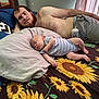 Wayden is registered to the contest to win money with this photo: baby, man, bed, pillow, bottle, striped_onesie, sunflower_pattern, sleeping, relaxing, indoor, curtains, shorts, beard, hair, skin, hand, face, person, clothing, furniture
