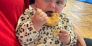 Skylar is registered to the contest to win money with this photo: baby, child, indoor, donut, food, eating, leopard_print, clothing, person, lap, hand, crumbs, floor, wooden_chair, stroller, toy, face, cute, sitting, casual