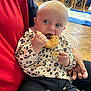 baby, child, indoor, donut, food, eating, leopard_print, clothing, person, lap, hand, crumbs, floor, wooden_chair, stroller, toy, face, cute, sitting, casual