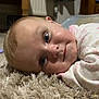 Skylar joined the competition — help win amazing prizes! baby, child, face, eyes, carpet, floor, indoor, furniture, wood, smile, clothing, pajamas, cozy, portrait, closeup, person, head, skin, room, curious