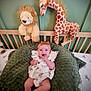 baby, plush_toy, lion, giraffe, crib, cushion, green, child, infant, smile, headband, dress, nursery, soft_toy, furniture, wooden, sleeping_area, cute, comfort, indoor