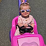 toddler, child, sunglasses, pink, toy_car, outdoor, paved_path, grass, sunny, pigtails, bows, smiling, steering_wheel, cute, playtime, summer, road, person, fashion, happy