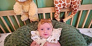 Nova joined the competition — help win amazing prizes! baby, infant, plush_toy, lion_toy, giraffe_toy, crib, cushion, green, headband, white_dress, patterned_clothing, child, indoors, nursery, soft_toys, smiling, cute, seated, decor, furniture