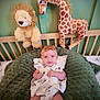 baby, infant, plush_toy, lion_toy, giraffe_toy, crib, cushion, green, headband, white_dress, patterned_clothing, child, indoors, nursery, soft_toys, smiling, cute, seated, decor, furniture