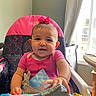 Jolynn is registered to the contest to win money with this photo: baby, child, high_chair, pink_bow, smiling, indoor, daylight, curtains, window, toy, colorful, person, infant, clothing, face, hand, cheerful, home, furniture, playtime