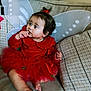 toddler, child, red_dress, fairy_wings, couch, cushions, indoors, sitting, curious, finger_in_mouth, hair_bow, cute, portrait, fabric, home, cozy, soft_lighting, baby, person, expression
