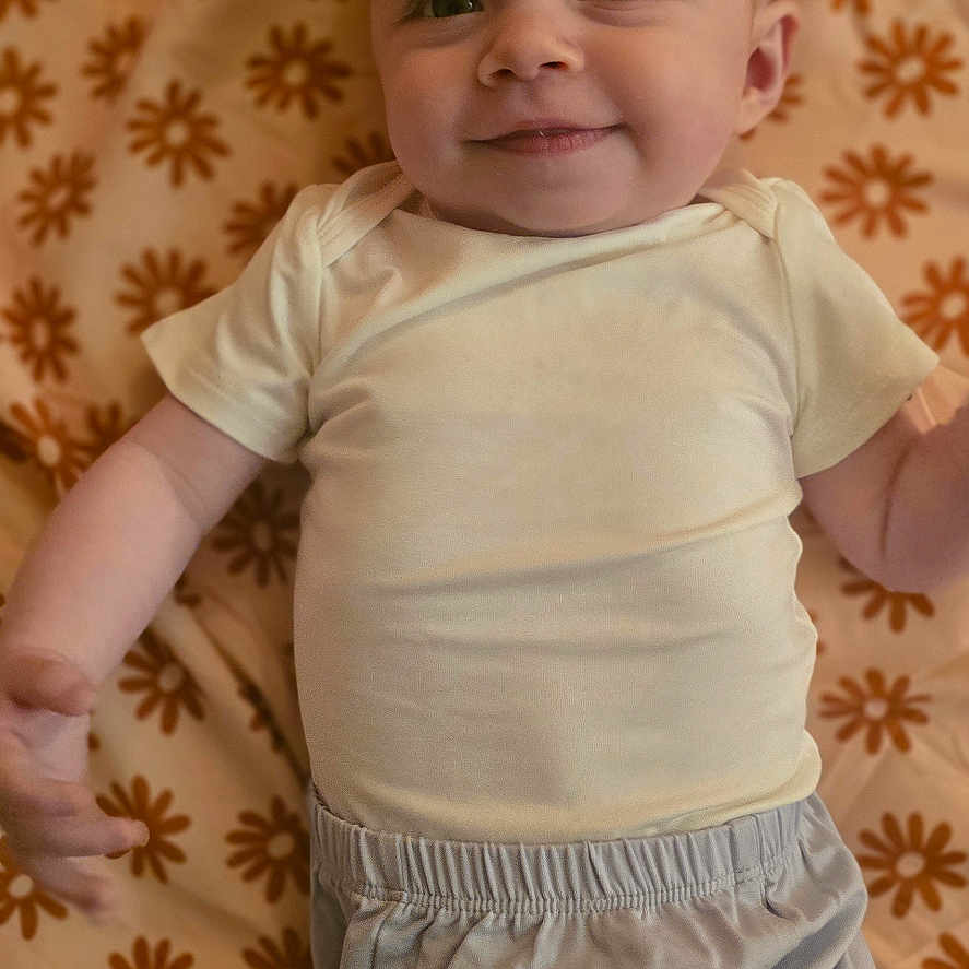 Skylar is registered to the contest to win money with this photo: baby, infant, smiling, face, person, lying_down, blanket, pattern, clothing, ponytail, cute, happy, child, young, indoors, fabric, casual, toddler, portrait, soft_lighting
