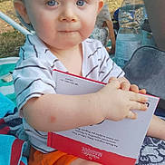 Noah participe au concours pour gagner de l'argent avec cette photo : baby, book, cap, child, curious, daylight, face, grass, hand, legs, nature, outdoor, picnic, shorts, sitting, striped_shirt, summer, toddler, towel, water_bottle