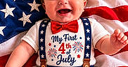 Sebastian is registered to the contest to win money with this photo: baby, child, smiling, patriotic, american_flag, red_bow_tie, suspenders, celebration, holiday, 4th_of_july, fireworks_graphic, clothing, infant, cute, portrait, lying_down, fabric, stars, stripes, happy