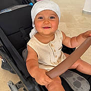 Ayaan participe au concours pour gagner de l'argent avec cette photo : baby, stroller, child, smiling, headwrap, indoor, seat, hand, clothing, button, safety_bar, floor, footwear, person, happy, infant, expression, holding, background, wheel