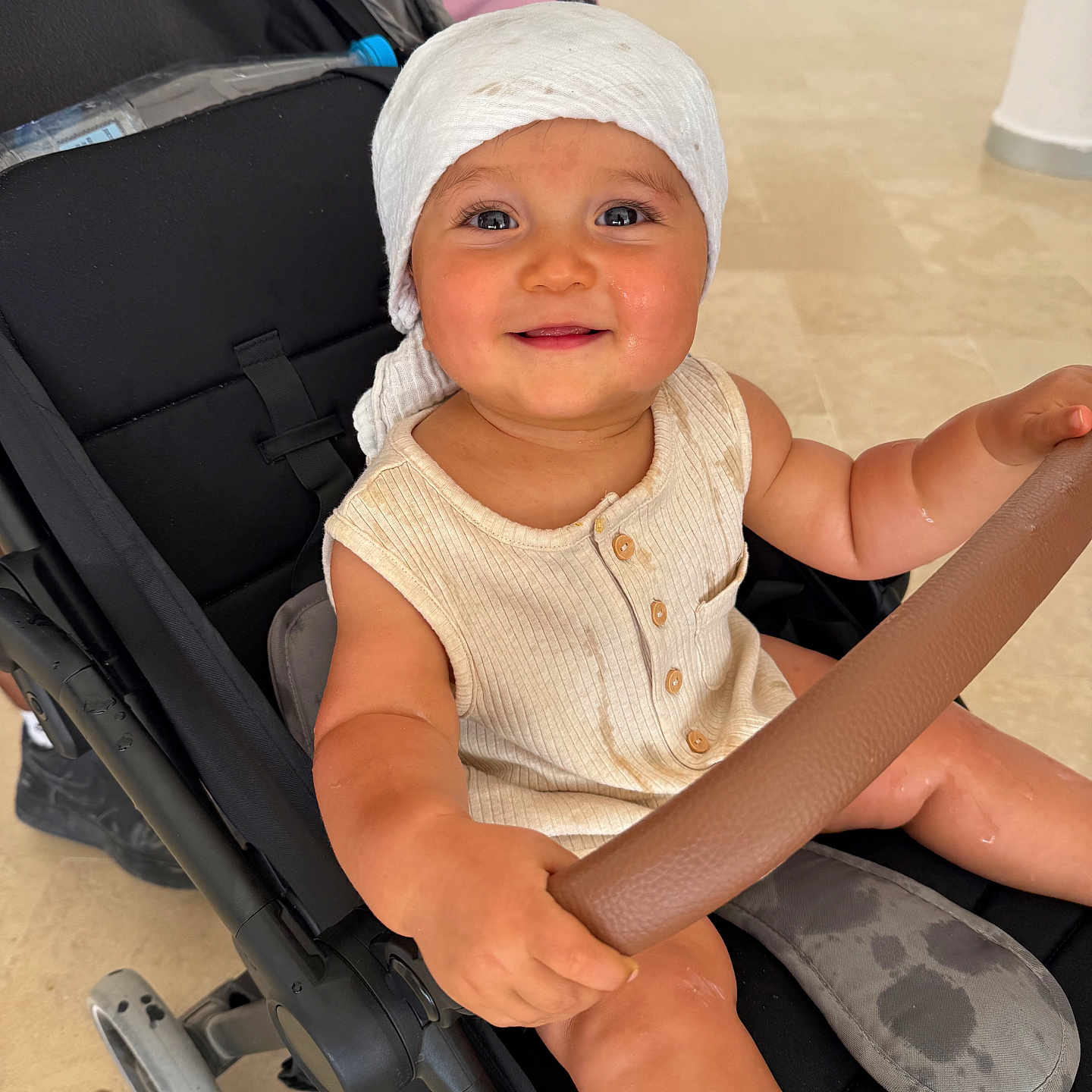 Ayaan participe au concours pour gagner de l'argent avec cette photo : baby, background, button, child, clothing, expression, floor, footwear, hand, happy, headwrap, holding, indoor, infant, person, safety_bar, seat, smiling, stroller, wheel