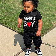 Chance is registered to the contest to win money with this photo: toddler, child, curly_hair, black_tshirt, mamas_boy, red_heart, black_pants, sneakers, sidewalk, grass, outdoor, sunny, shadow, standing, casual_clothing, young_child, person, cute, portrait, daytime